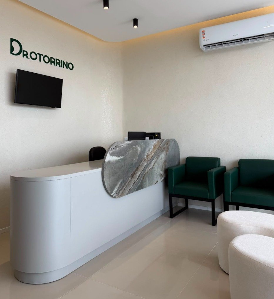 Recepção da clínica vista de frente, com balcão, logotipo e poltronas verdes